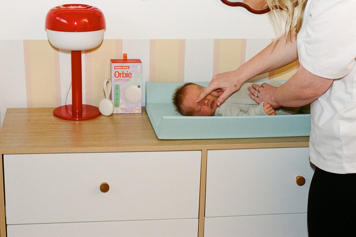 A parent changing a baby on a change table beside a red lamp and the Orbie box