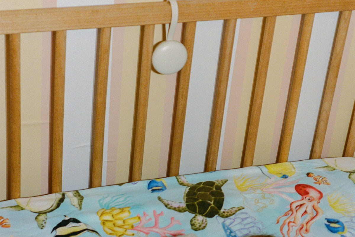 Orbie hanging from a wooden cot rail above a sea-creature cot sheet