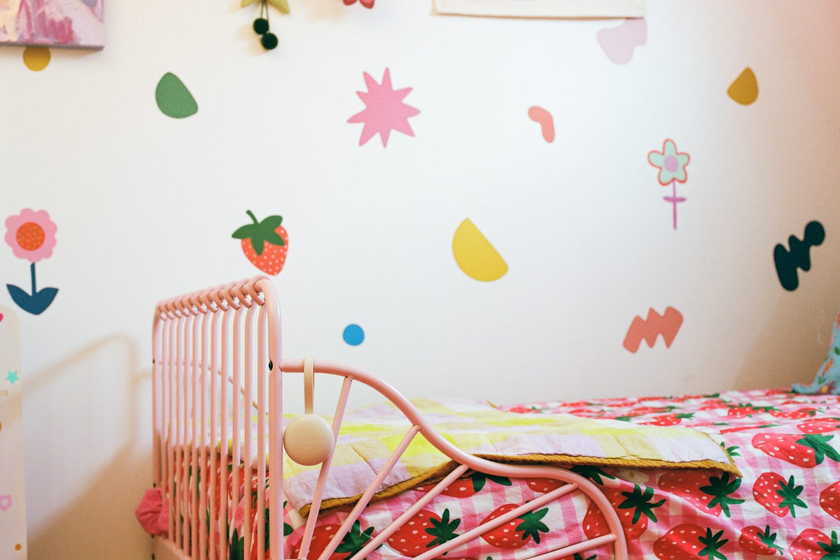 A nursery wall with decals and a pink toddler bed, Orbie on the rail