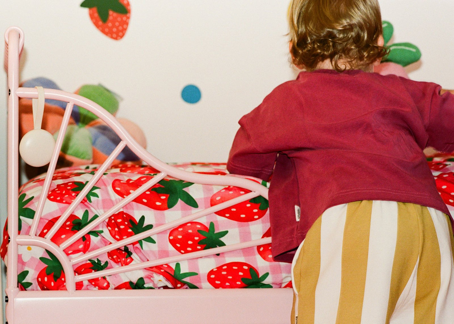 A toddler climbing on a strawberry-print bed